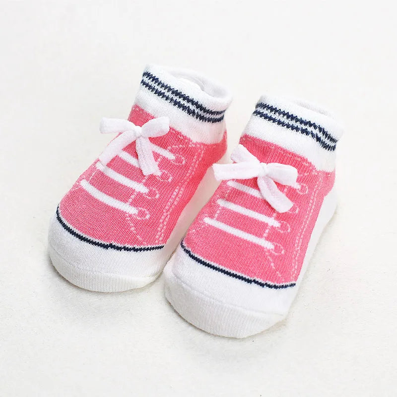 Pair of pink baby socks styled like sneakers with white bows and navy stripes, featuring anti-slip soles for safe walking and crawling.
